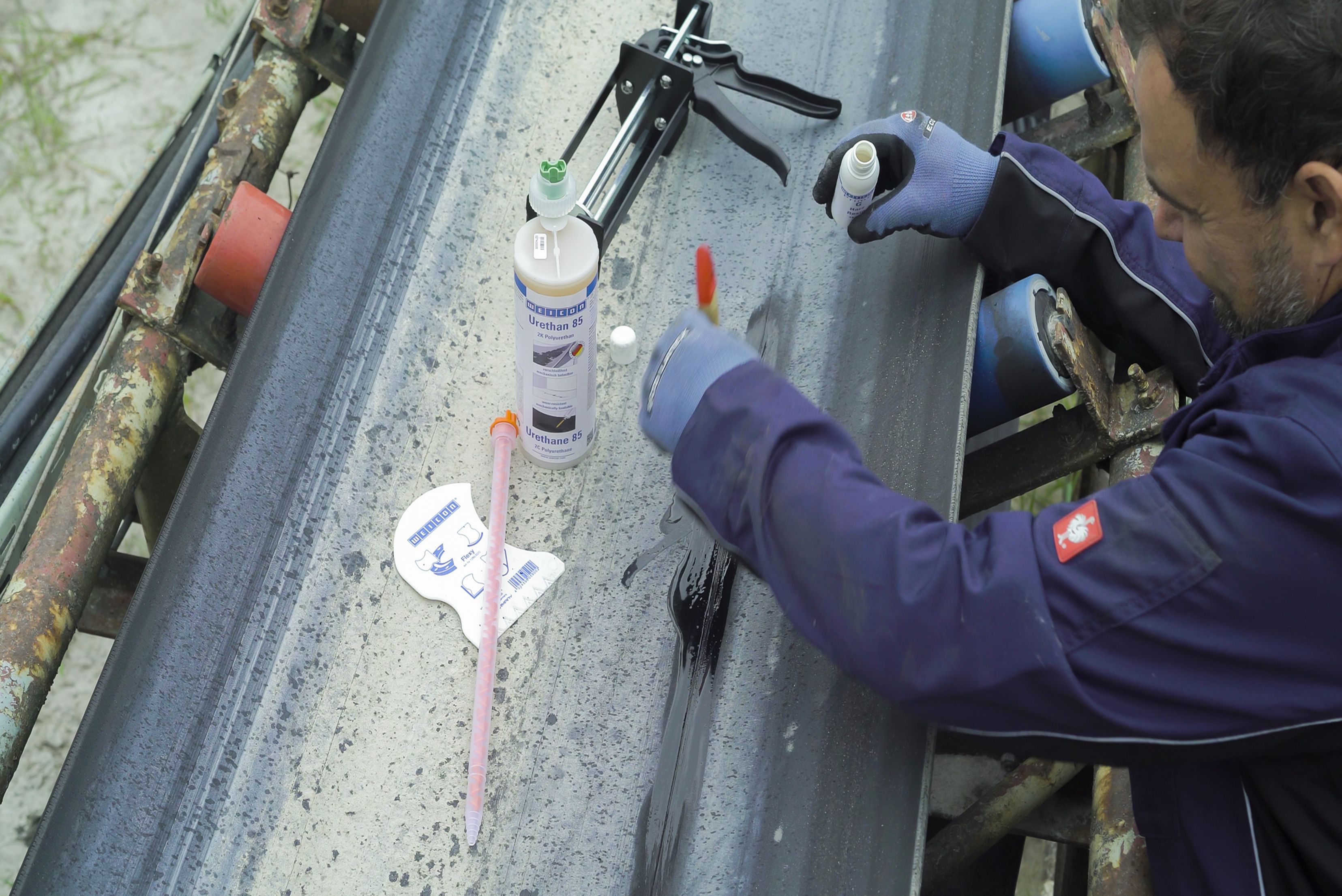 Un operaio applica un primer o una sostanza liquida con un pennello su un nastro trasportatore da riparare.