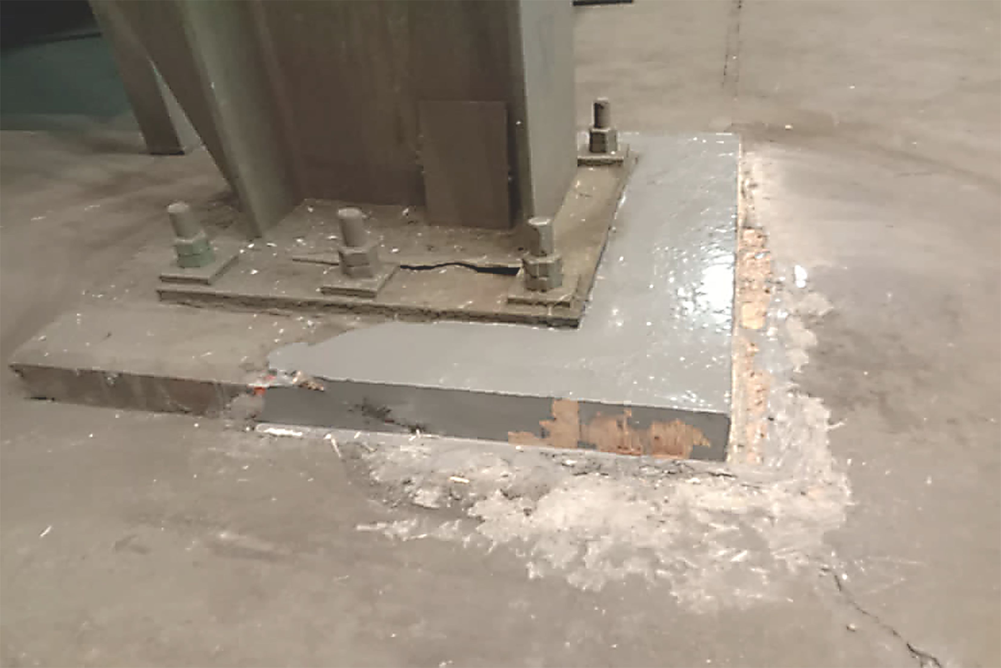 Base di macchinario industriale in calcestruzzo riparata e livellata con una resina grigia attorno ai bulloni d'ancoraggio.