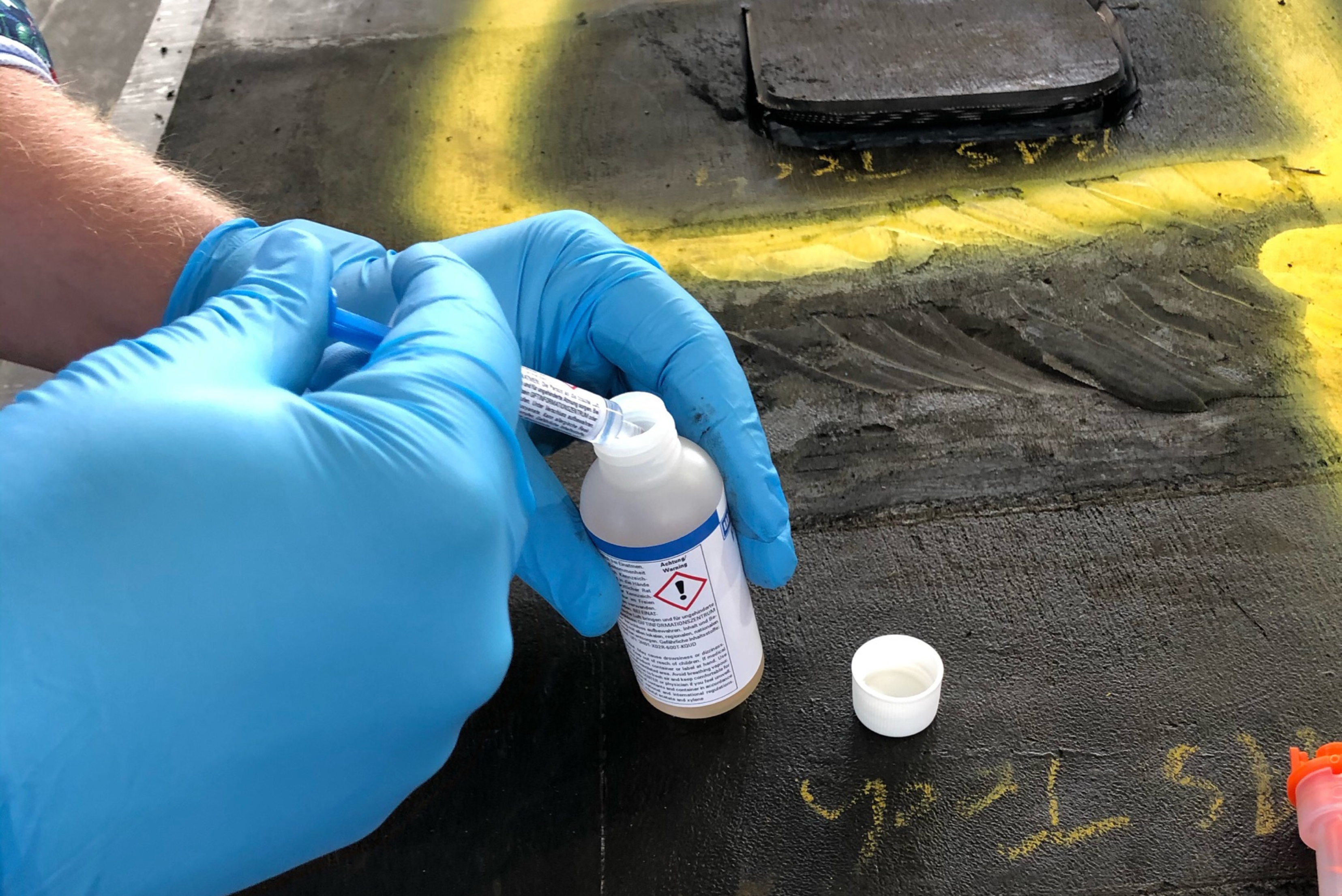 Una persona con guanti azzurri utilizza una siringa per prelevare del liquido da un flacone di reagente chimico.