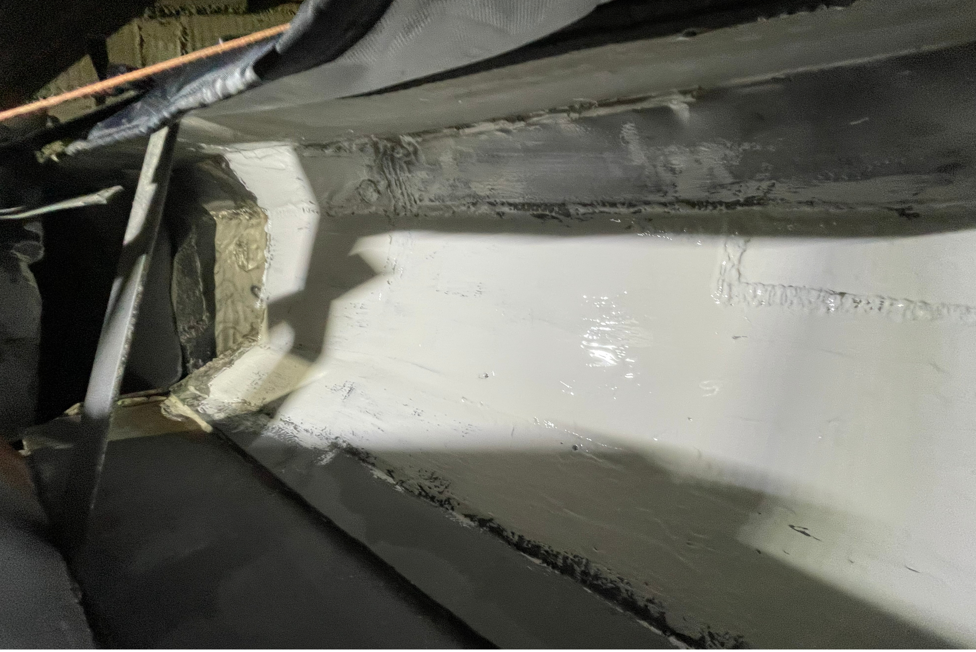 Una superficie metallica industriale interna trattata con un rivestimento protettivo liscio e chiaro, che mostra bordi sigillati e zone angolari accuratamente riparate.