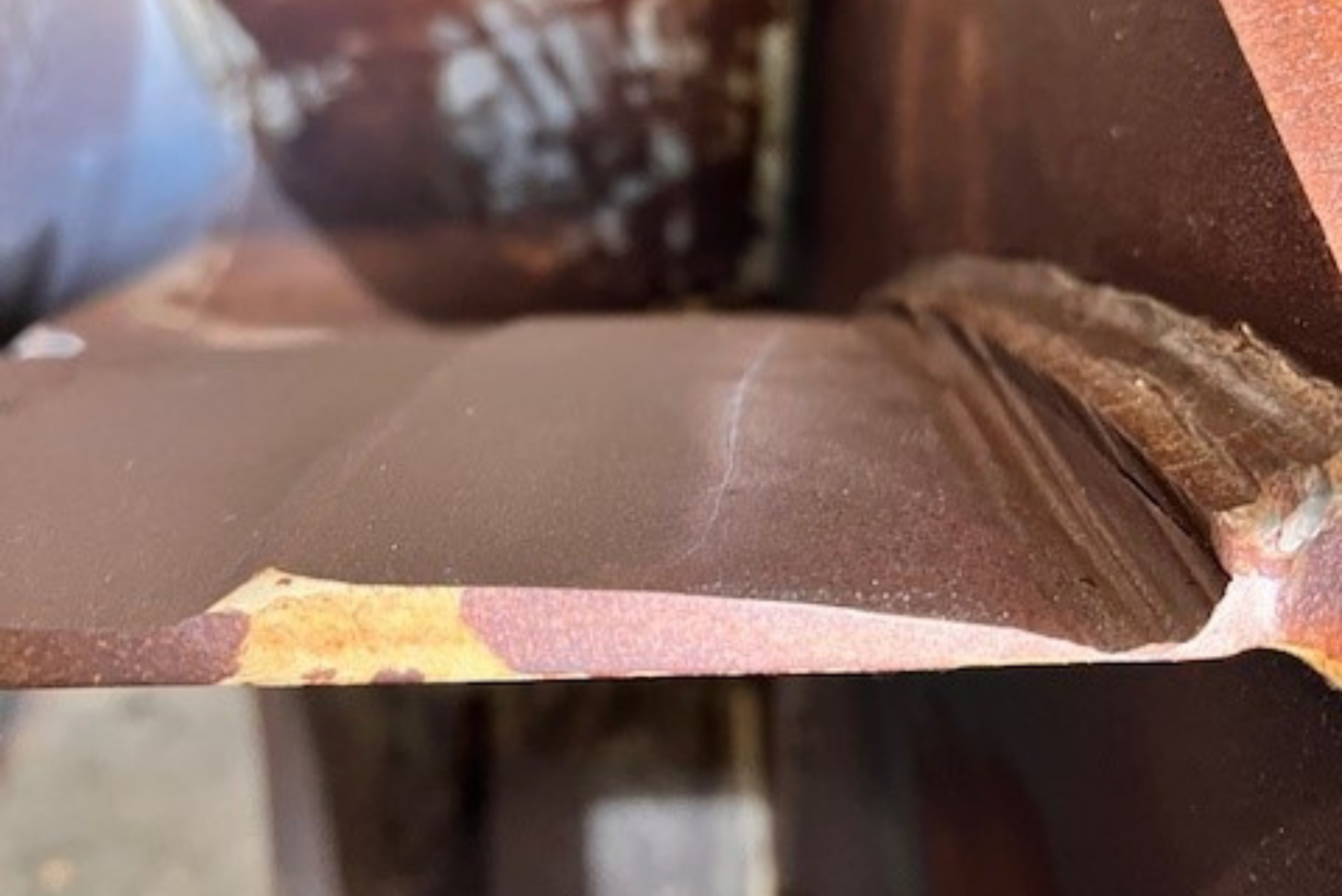 Primo piano di una crepa superficiale su un componente metallico industriale arrugginito vicino a un cordone di saldatura.
