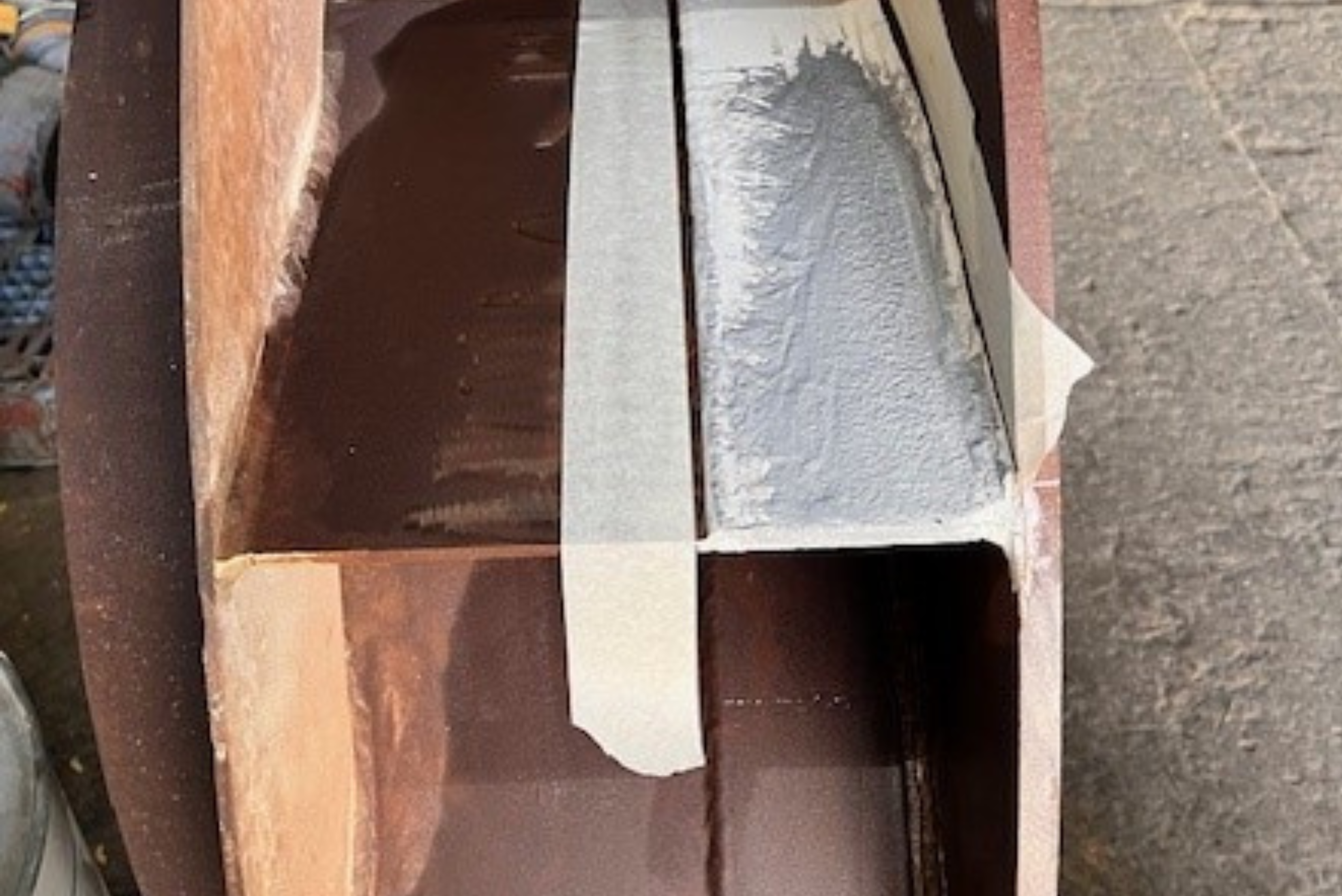 Un componente metallico industriale delimitato da nastro adesivo da carrozziere, con un'area riparata mediante resina epossidica grigia.
